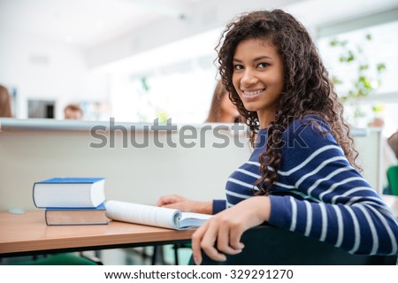 Portrait of a happy female student sitting at the desk in university and looking at camera