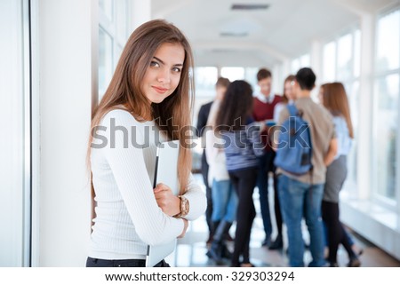 Portrait of a happy female student standing in university hall with classmates on background