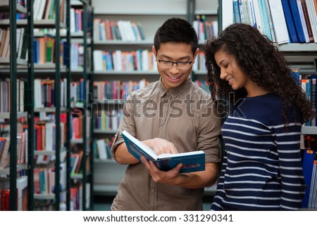 Portrait of a happy students searching book in library together