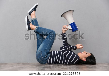 Young beautiful happy smiling woman lying with legs up and speaking in megaphone