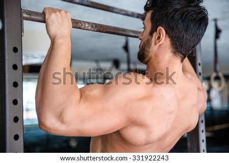 Back view portrait of a muscular man tightening on horizontal bar at gym