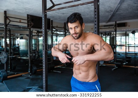 Portrait of a mucular male bodybuilder resting near parallel bars in fitness gym and looking at camera