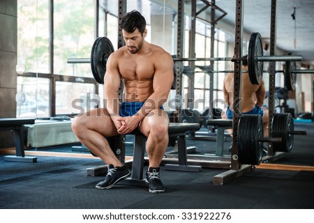 Portrait of a muscular man resting on the bench in fitness gym