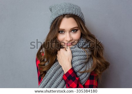 Portrait of a smiling cute woman with scarf and hat standing over gray background and looking at camera