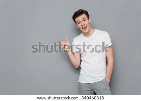 Portrait of handsome inspired attractive casual male in white t-shirt and gray pants pointing away on copyspace
