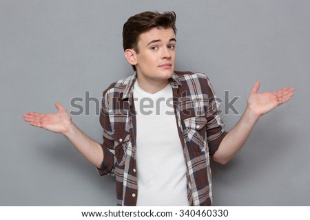 Portrait of handsome unshure confused puzzled man shrugging shoulders isolated over gray background