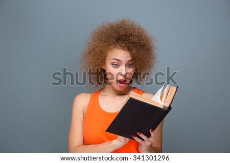 Wondered curly smart surprised young amazed female reading book over gray background