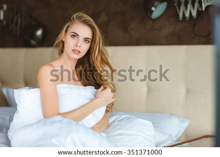Beautiful sensual young female sitting on bed wrapped in white duvet