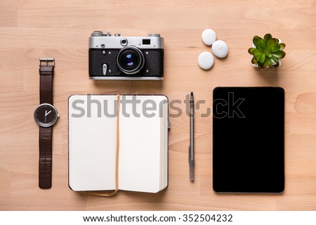 Top view of opened blank notepad, pen, watch, vintage camera, tablet and flower on wooden background