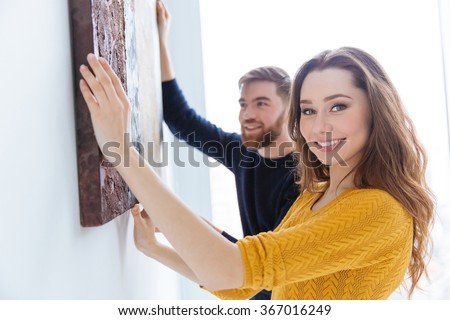 Cheerful couple hanging picture on the wall at home