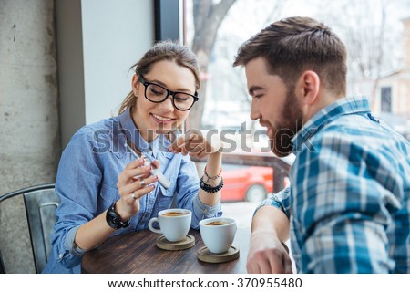 Happy couple using smartphone together and drinking coffee in cafe