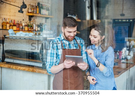 Smiling handsome waiter holding tablet and young pretty woman pointing on it in coffee shop