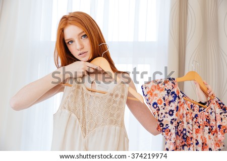 Pensive beautiful young woman desiding what to wear and choosing dress at home