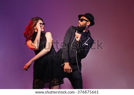 Multiethnic young couple in glasses dancing and having fun over colorful background