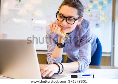 Happy attractive business woman in glasses standing and working with laptop in office