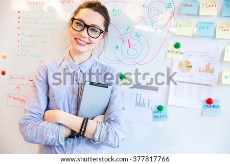 Happy businesswoman in glasses looking at camera with whiteboard on background