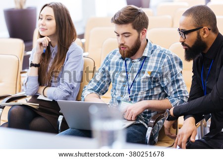 Multiethnic group of young business people using laptop sitting on meeting in conference hall