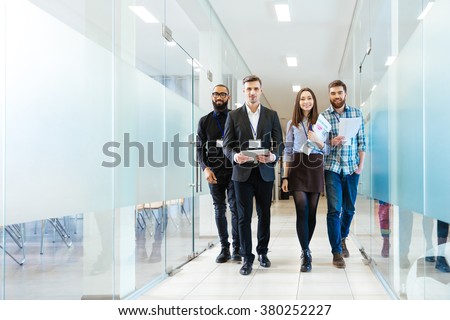 Full length of group of happy young business people walking the corridor in office together