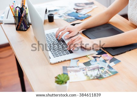 Closeup of hands of young woman photograper typing on laptop keyboard and using graphic tablet
