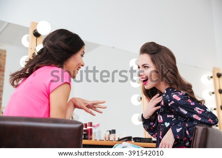 Two excited wondered young women talking near the mirror in beauty salon
