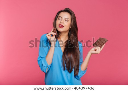 Sensual attractive young woman eating chocolate over pink background