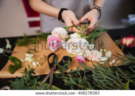 Closeup of hands of young woman florist creating bouquet of pink roses on the table