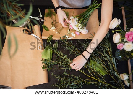 Top view of hands of young woman florist creating bouquet of flowers on black table