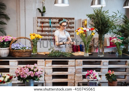 Cute concentrated young female florist in glasses working in flower shop