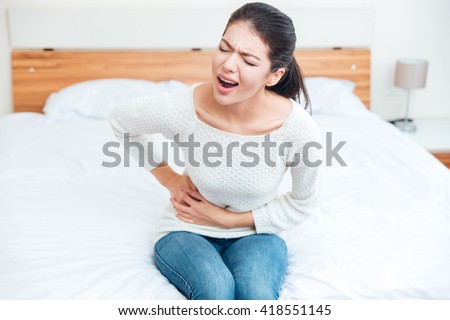 Woman sitting on the bed and touching her left side in pain at home