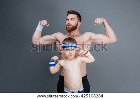 Strong bearded man and his son standing and showing biceps over grey background