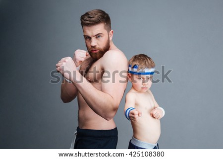 Portrait of athletic bearded father and his little son ready to fight over grey background