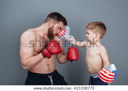 Dad and son playing using boxing gloves together over grey background