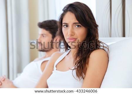 Unhappy upset woman sitting in the bed with man on the back at home
