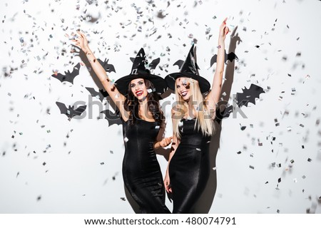 Two happy young women in black witch halloween costumes on party over white background