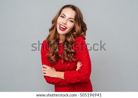 Cheerful beautiful young woman in red sweater over gray background
