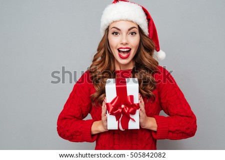 Happy excited young woman in santa claus hat with gift box over gray background