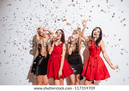 Four cheerful beautiful young women dancing and eating cupcakes on the party over white background