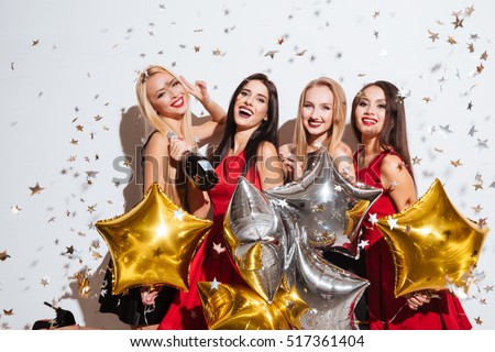 Four cheerful women with star shaped balloons and confetti drinking champagne and having party over white background
