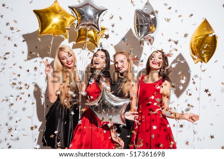 Four happy joyful young women with star shaped balloons and confetti having party over white background