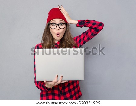 Portrait of a funny woman holding laptop computer and looking at camera over gray background