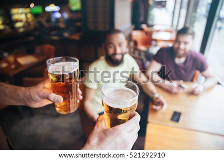 Closeup of waiter bringing two glasses of beer for two smiling bearded men sitting in pub