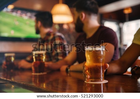 Closeup of three young men sdrinking beer in bar and watching football match