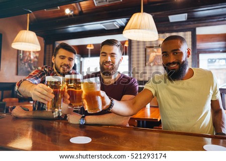 Three smiling handsome young friends drinking beer in bar together
