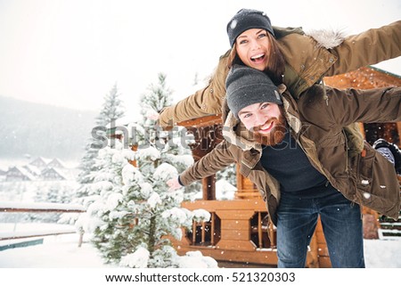 Happy handsome bearded man piggibacking his girlfriend and laughing in winter