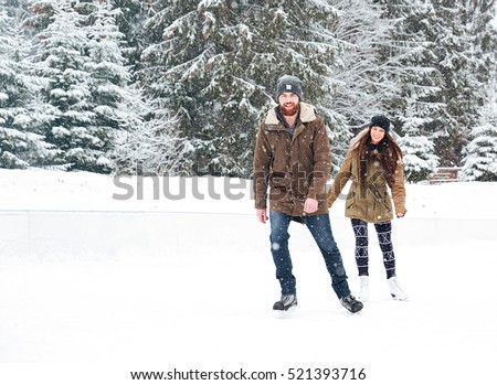 Smiling young couple ice skating outdoors with snow on background