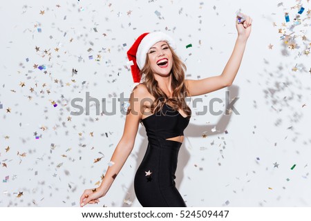 Happy excited young woman in santa claus hat dancing and laughing over white background