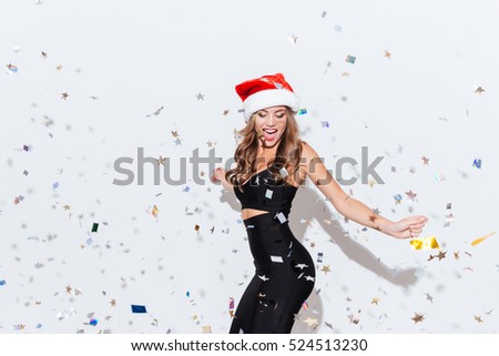 Cheerful attractive young woman in santa claus hat dancing and having fun over white background