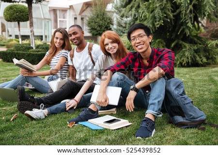 Multiethnic group of happy young people reading books on lawn outdoors
