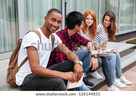 Happy african american young man student sitting with his friends outdoors