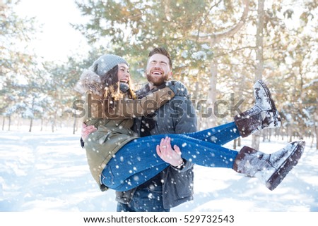Happy man holding his girlfriend on hands in winter park